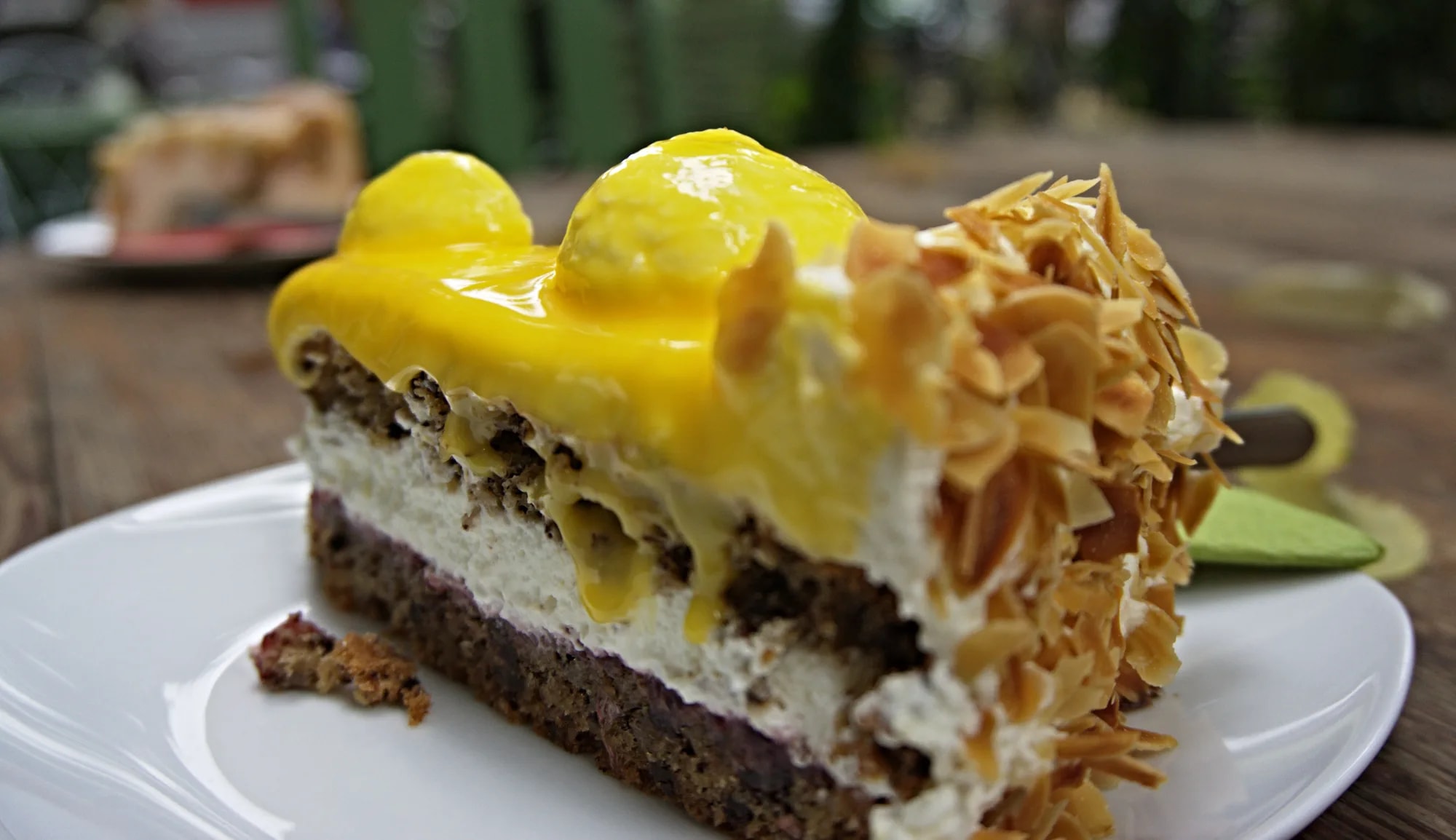 A slice of cheesecake with a lemon topping and almond flakes on a plate