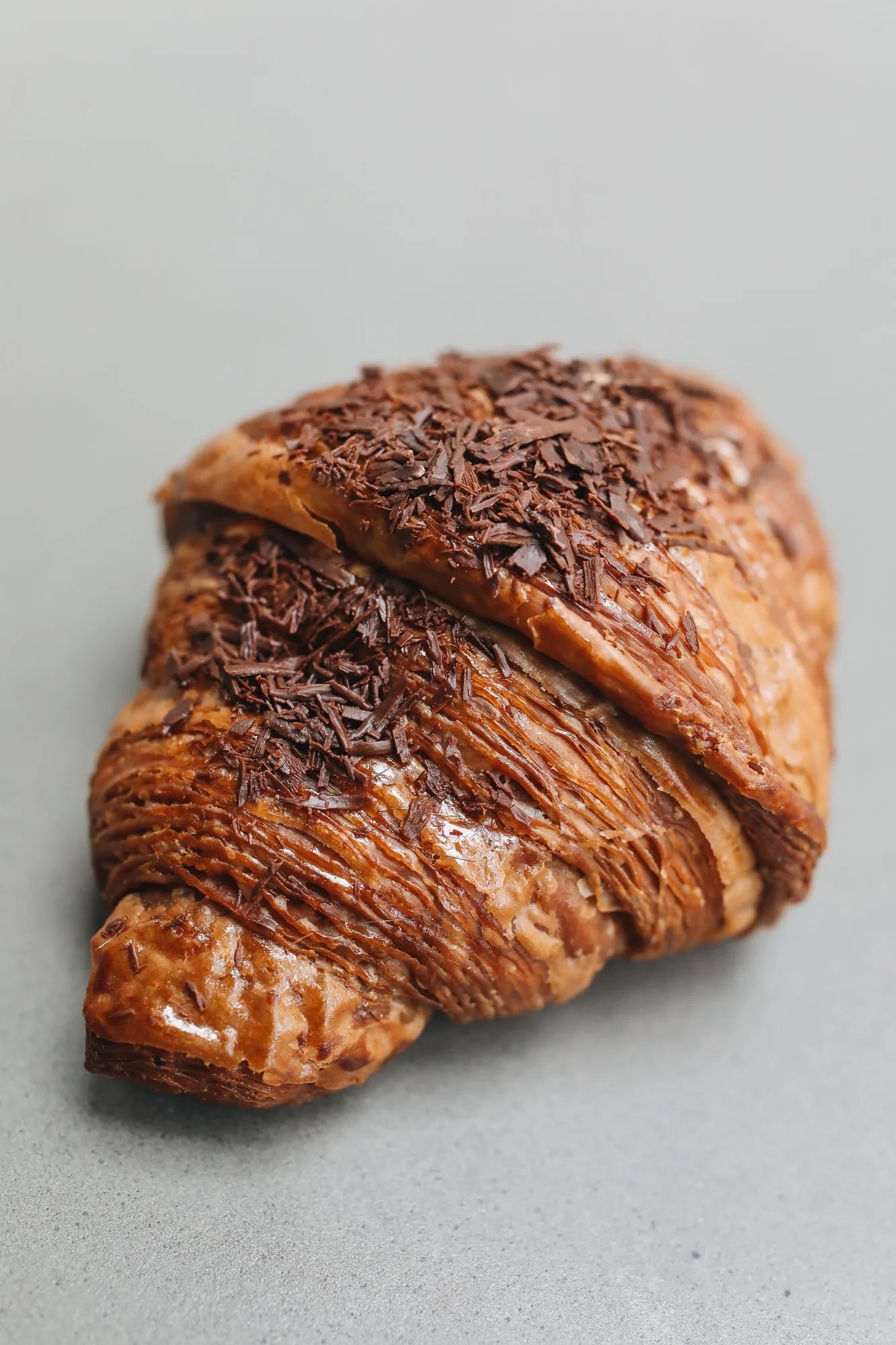 Close-up of a chocolate croissant (pain au chocolat) with visible chocolate filling on a grey surface