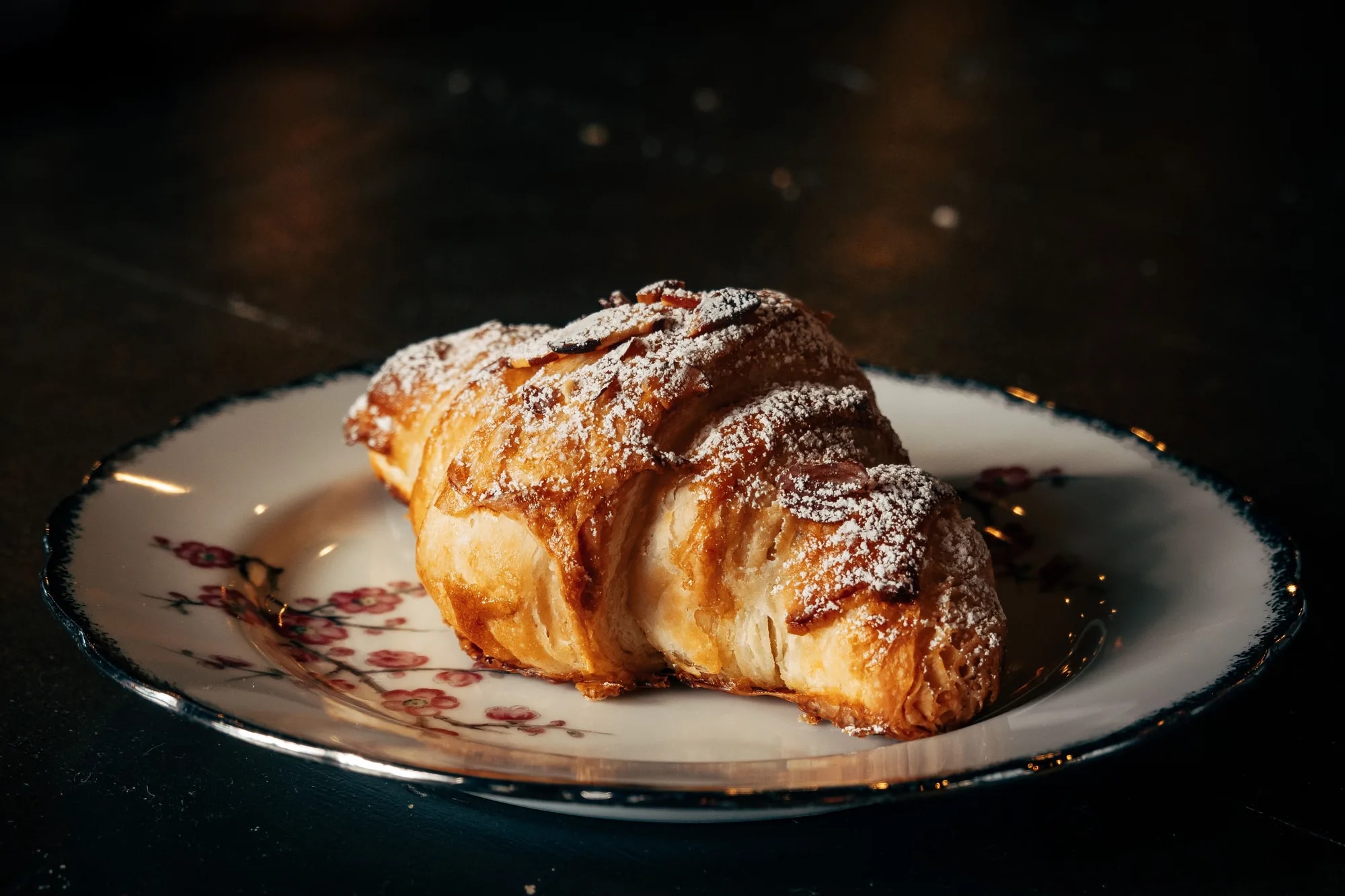 A freshly baked plain croissant dusted with powdered sugar on a plate