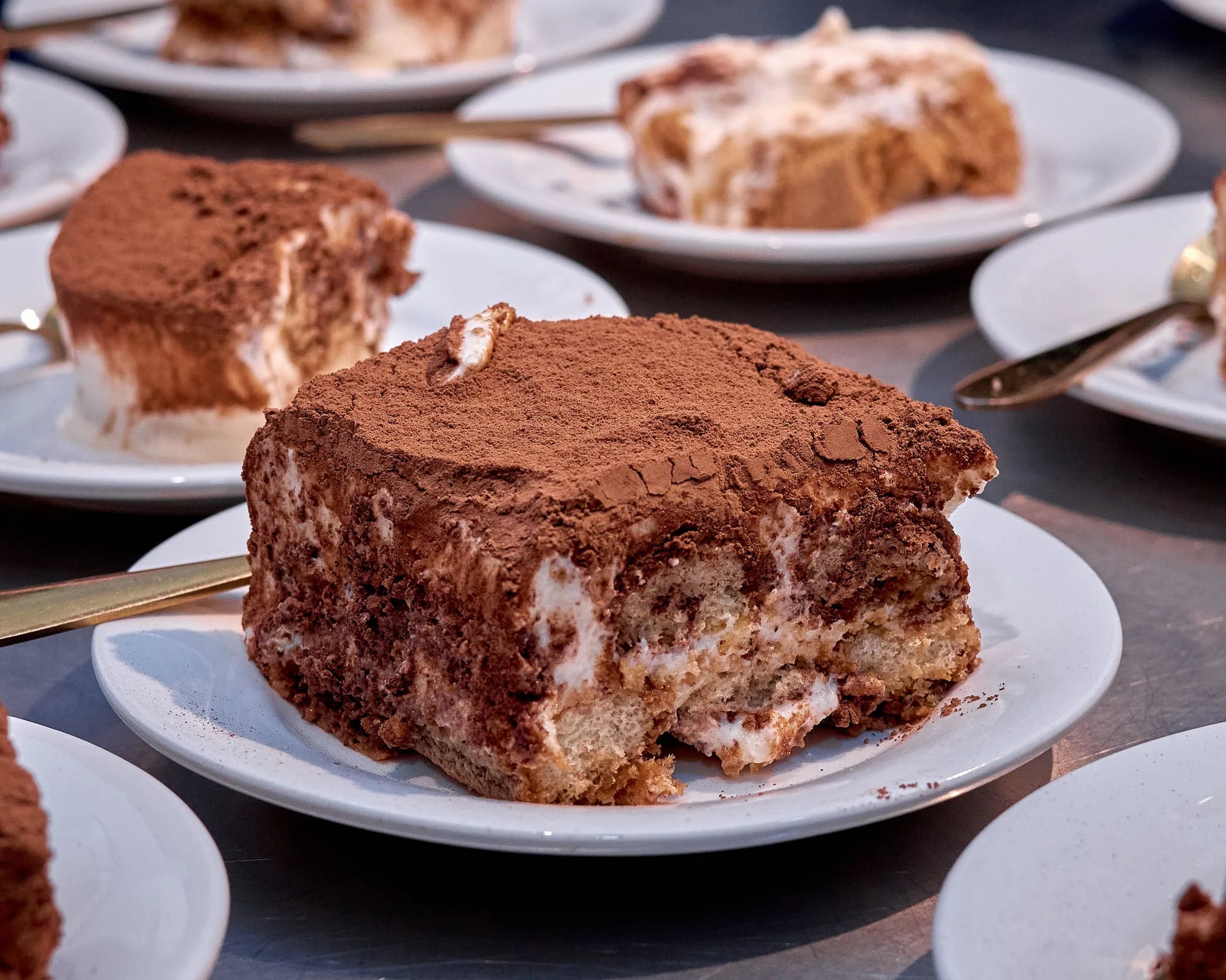 A slice of tiramisu dusted with cocoa powder on a white plate
