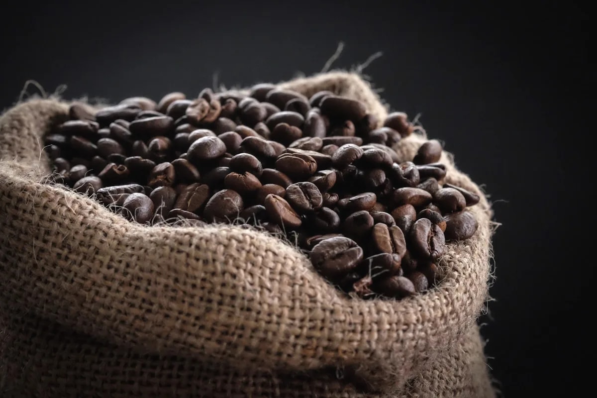 Roasted coffee beans overflowing from a burlap sack against a dark background