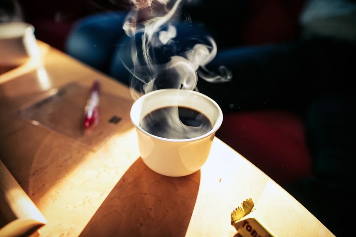 A plain white coffee cup sitting on a table in warm natural sunlight