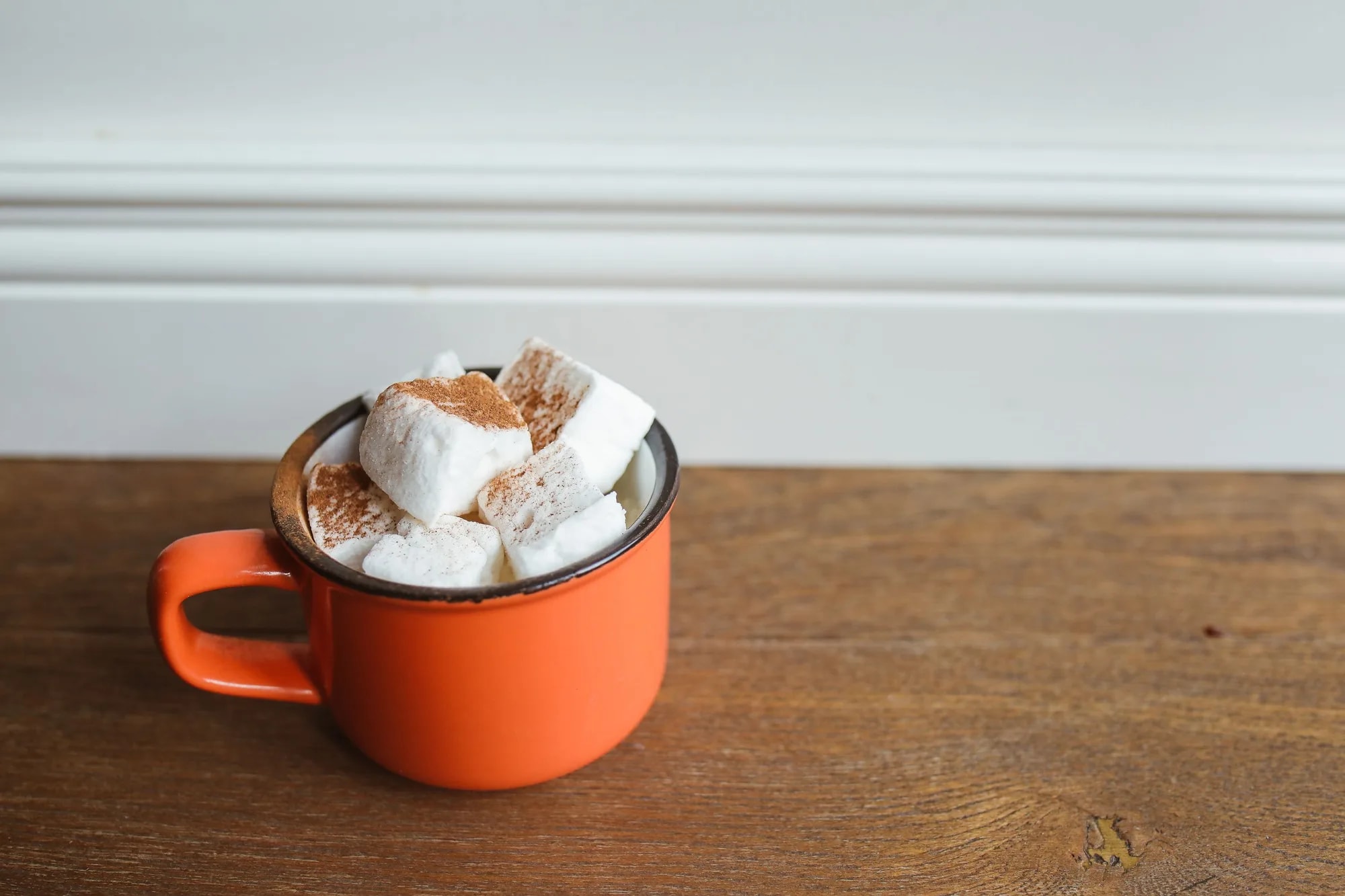 An orange ceramic mug of hot chocolate topped with fluffy marshmallows