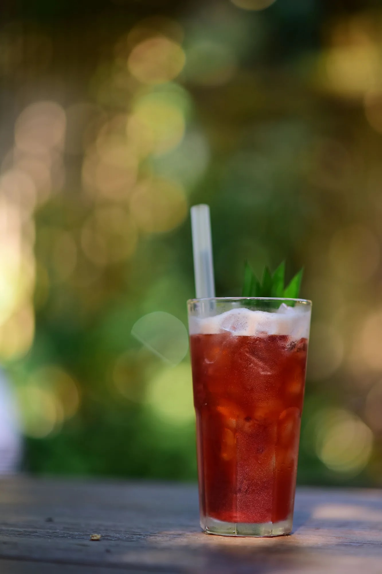 A tall glass of chilled deep-red hibiscus (karkade) iced tea garnished with fresh herbs