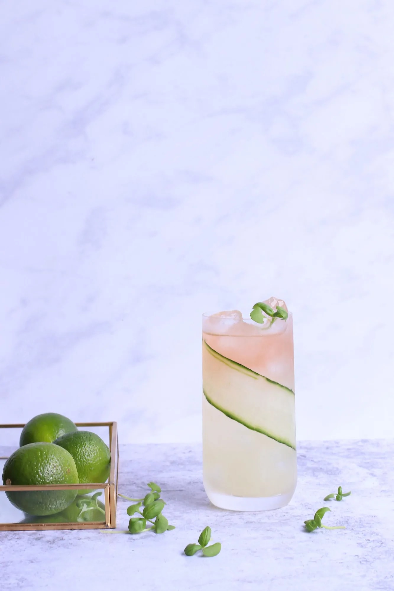 A glass of iced lemonade garnished with fresh mint, cucumber, and lime slices