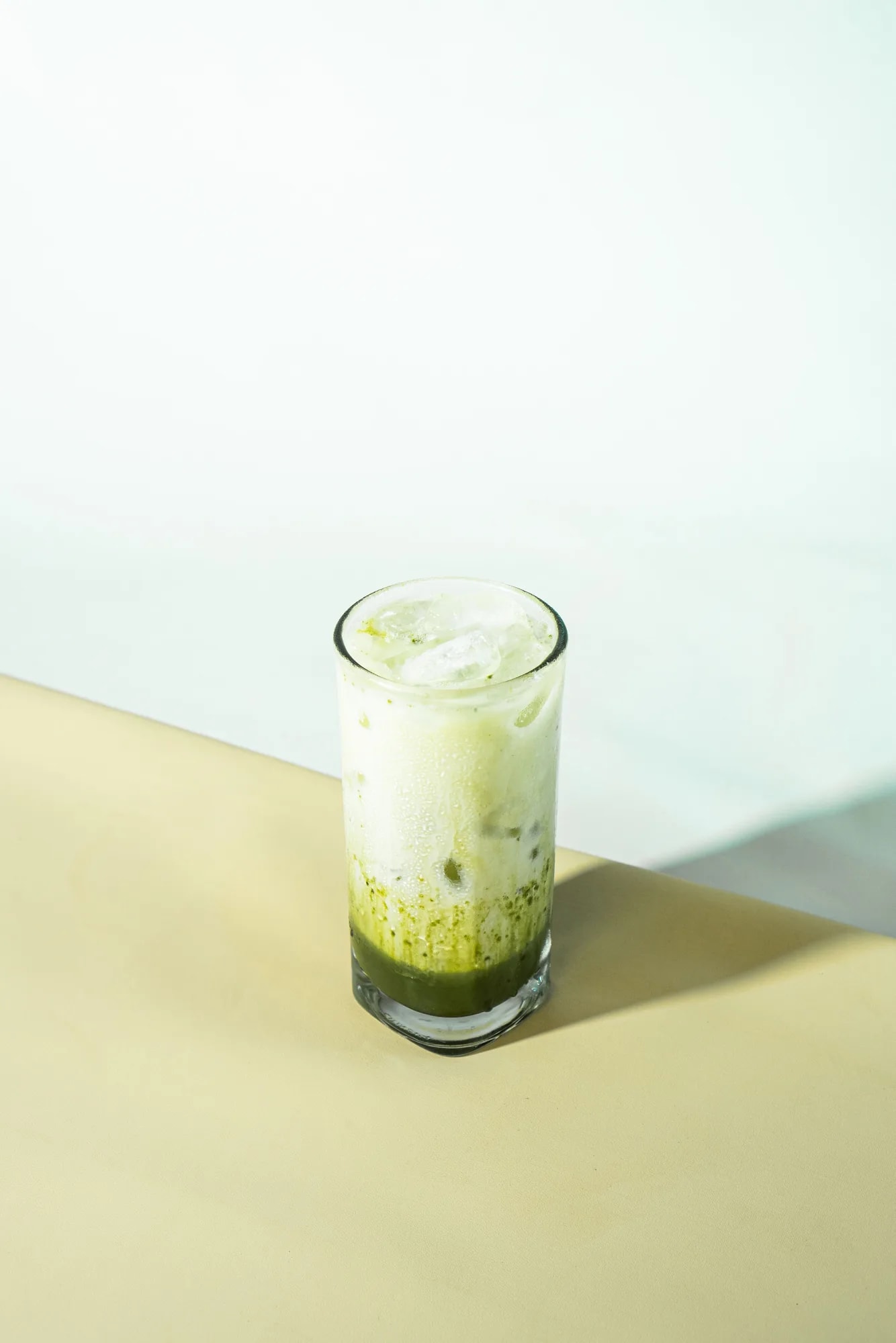 A tall glass of iced matcha latte with a frothy green top against a plain light background