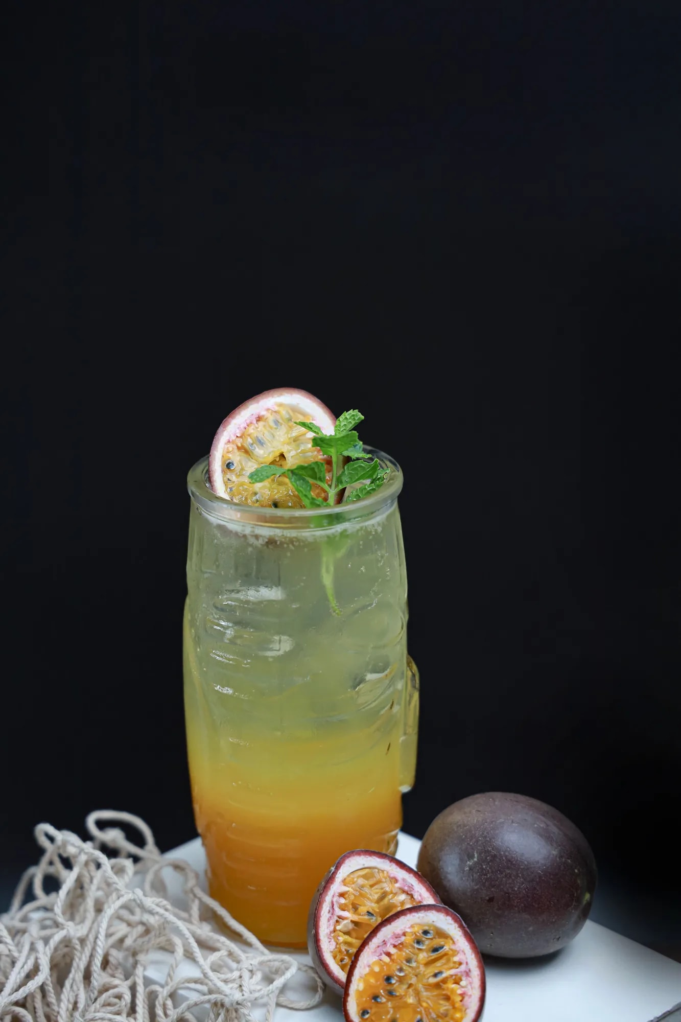 A golden-yellow passion fruit drink in a glass garnished with mint and a lime slice
